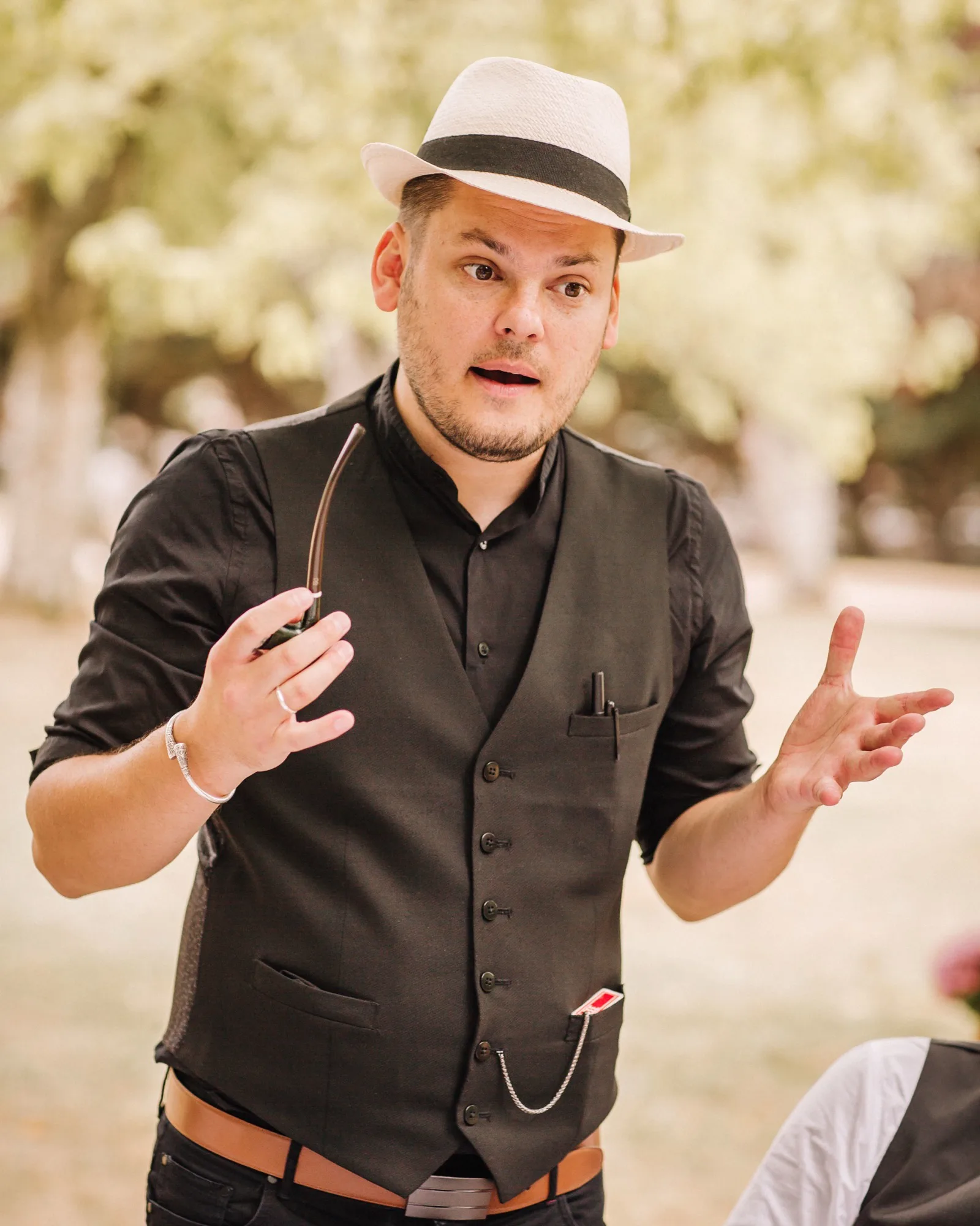 Jérôme en gilet et chapeau, mains ouvertes en pleine narration, sous les arbres